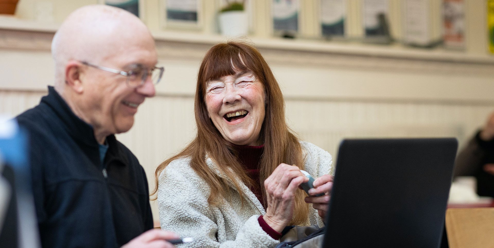 Zwei Senioren sitzen fröhlich vor einem Computer